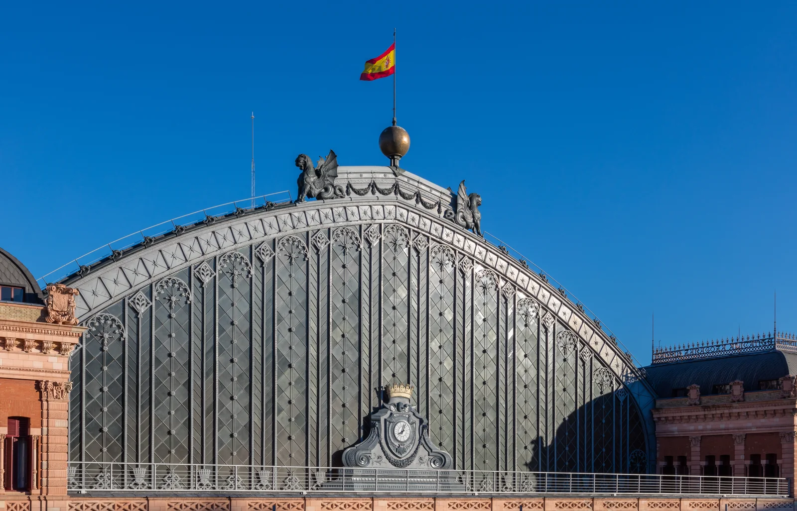 Fachada histórica de Atocha con arco de hierro, reloj y bandera sobre el tejado